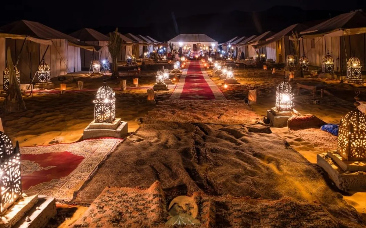 Von innen beleuchtete Zelte eines Wüstencamps zwischen hohen Sanddünen bei Nacht
