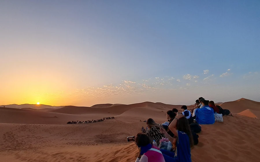 Ein Wüstencamp aus dunklen Zelten in einer Mulde zwischen hohen Sanddünen