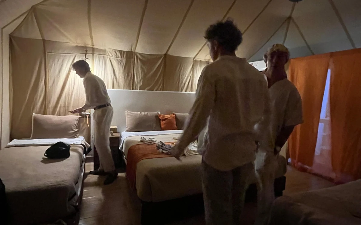 El interior de una tienda de campaña de lona en el desierto, con alfombras, mantas y una cama hecha